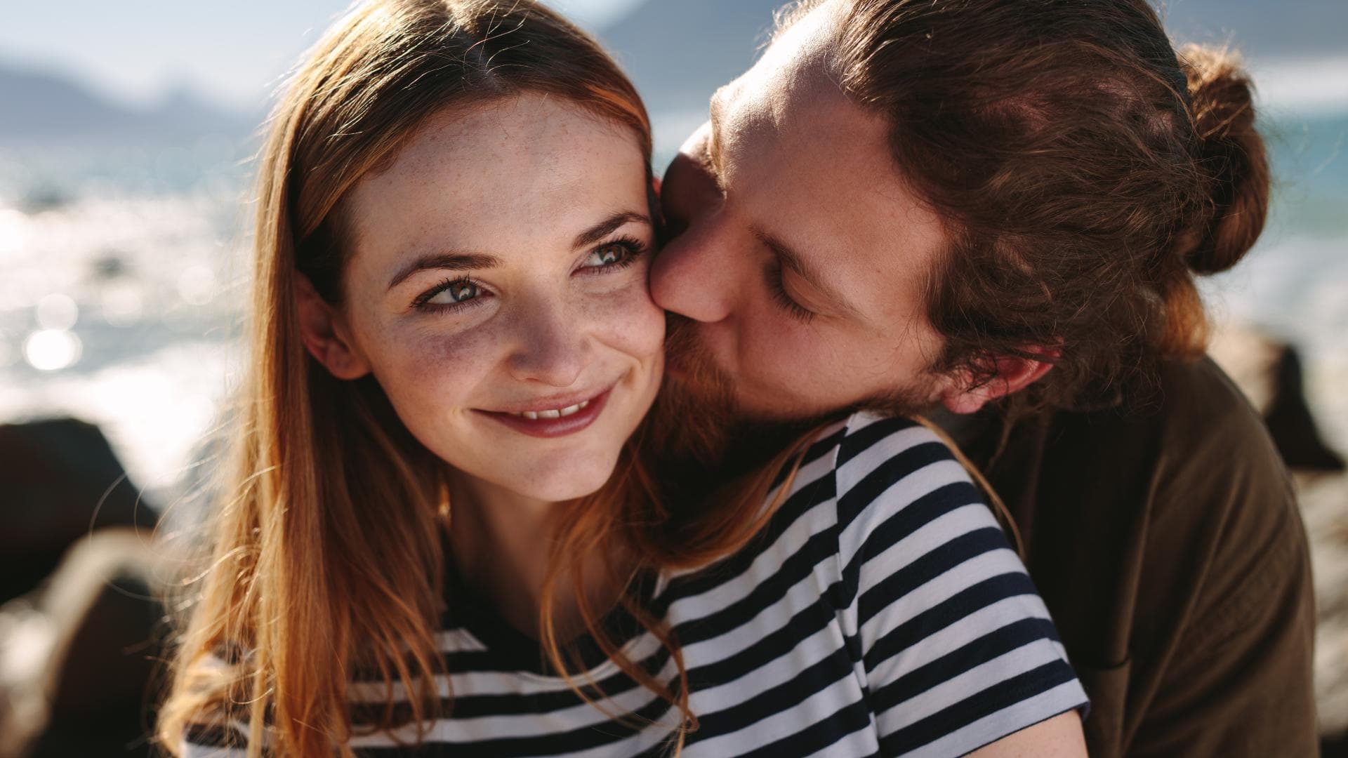 Liebe gestehen: Mit diesen Tipps schaffst du es Liebe gestehen: Mann umarmt Frau mit roten Haaren und gestreiftem T-Shirt