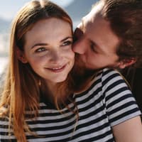 Liebe gestehen: Mit diesen Tipps schaffst du es Liebe gestehen: Mann umarmt Frau mit roten Haaren und gestreiftem T-Shirt