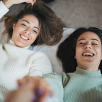 Ja Nein Fragen gegen Langeweile Zwei Freundinnen liegen im Bett und lachen